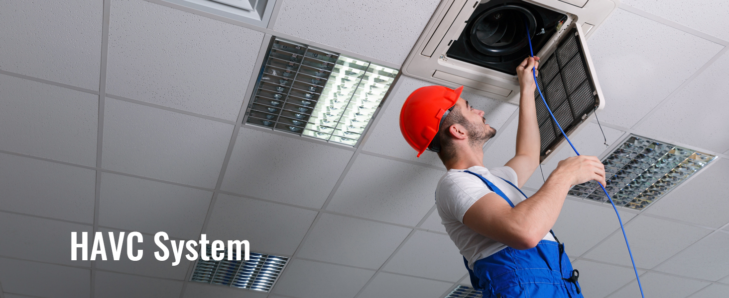 technician servicing havc system on ceiling with tools, wearing red hard hat and blue overalls.