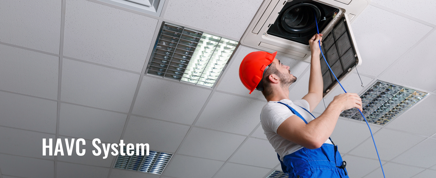 technician working on hvac system in ceiling, wearing red hard hat and blue overalls.